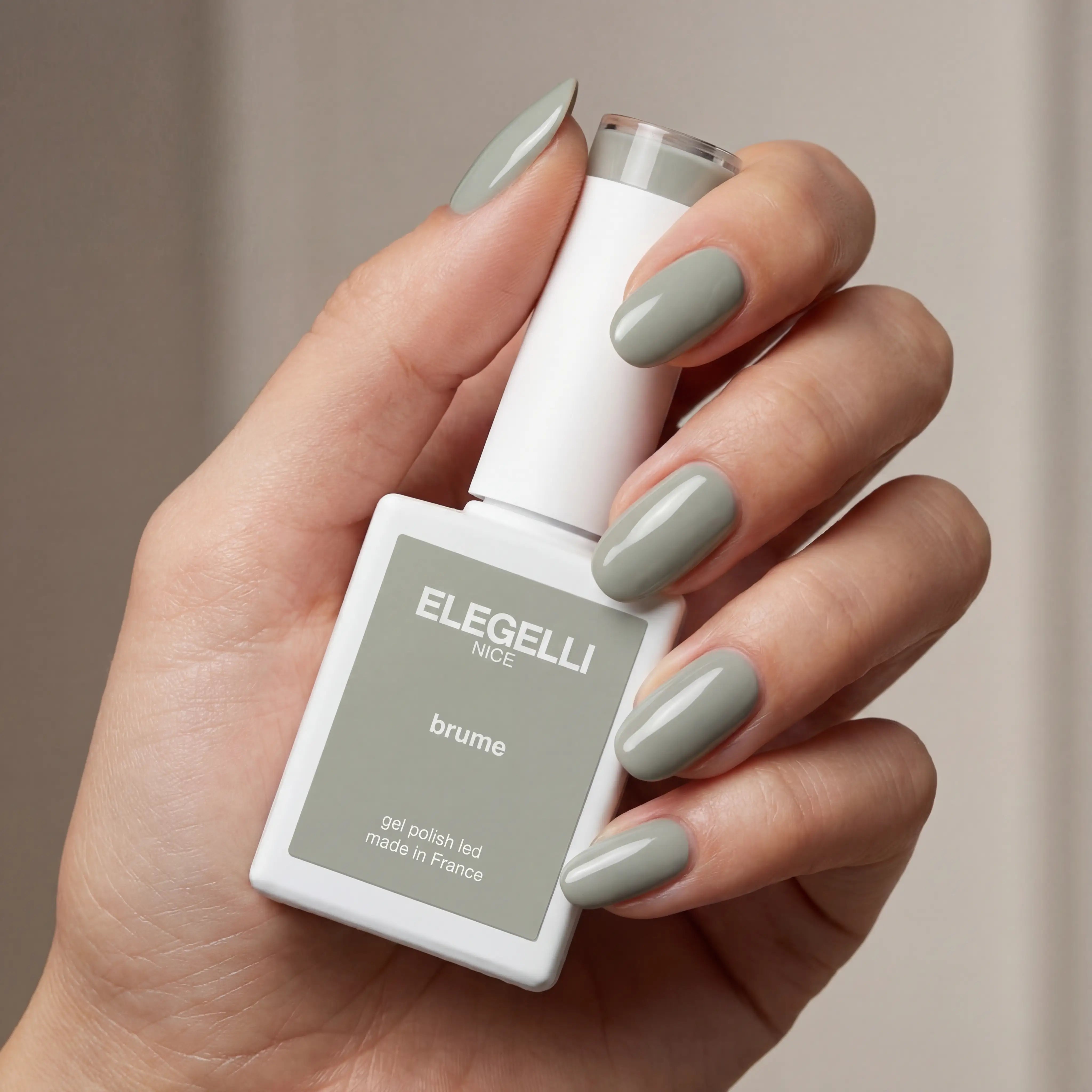 Hand holding a bottle of ELEGELLI nail polish with matching nails against a neutral background