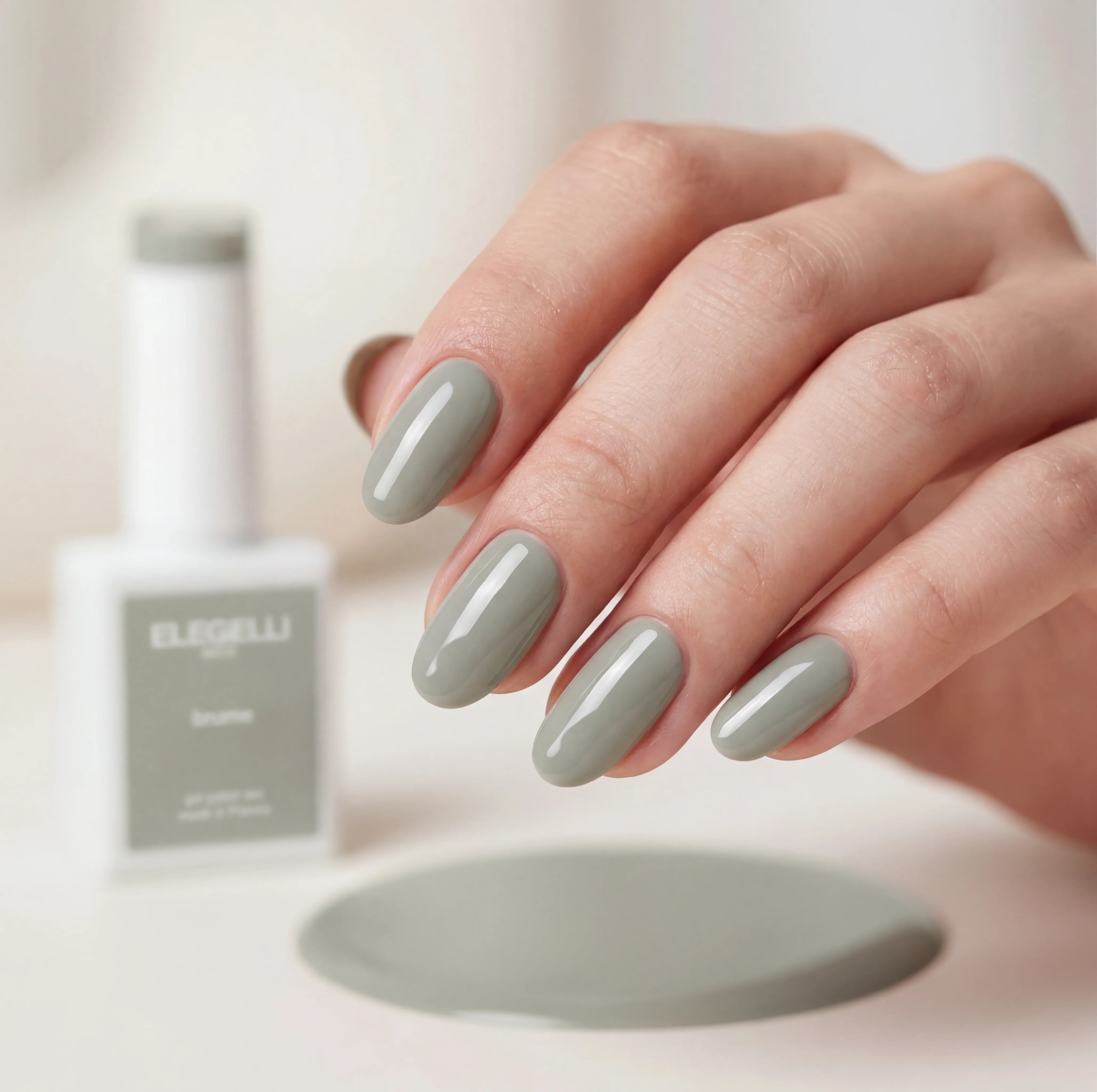 Hand with gray nail polish holding a bottle of ELEGELLI nail polish.
