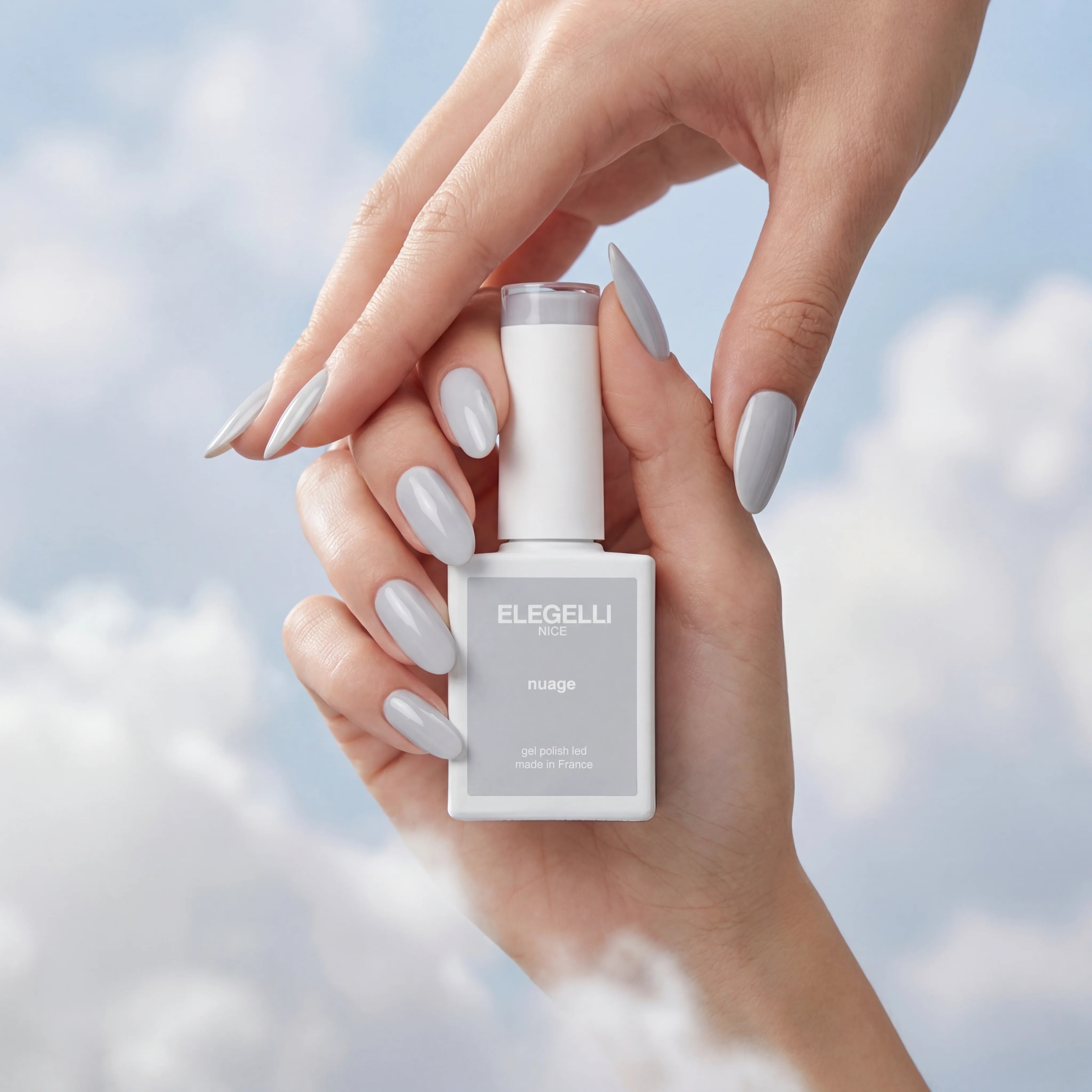 Hand holding a bottle of ELEGELLI nail polish against a cloudy sky background